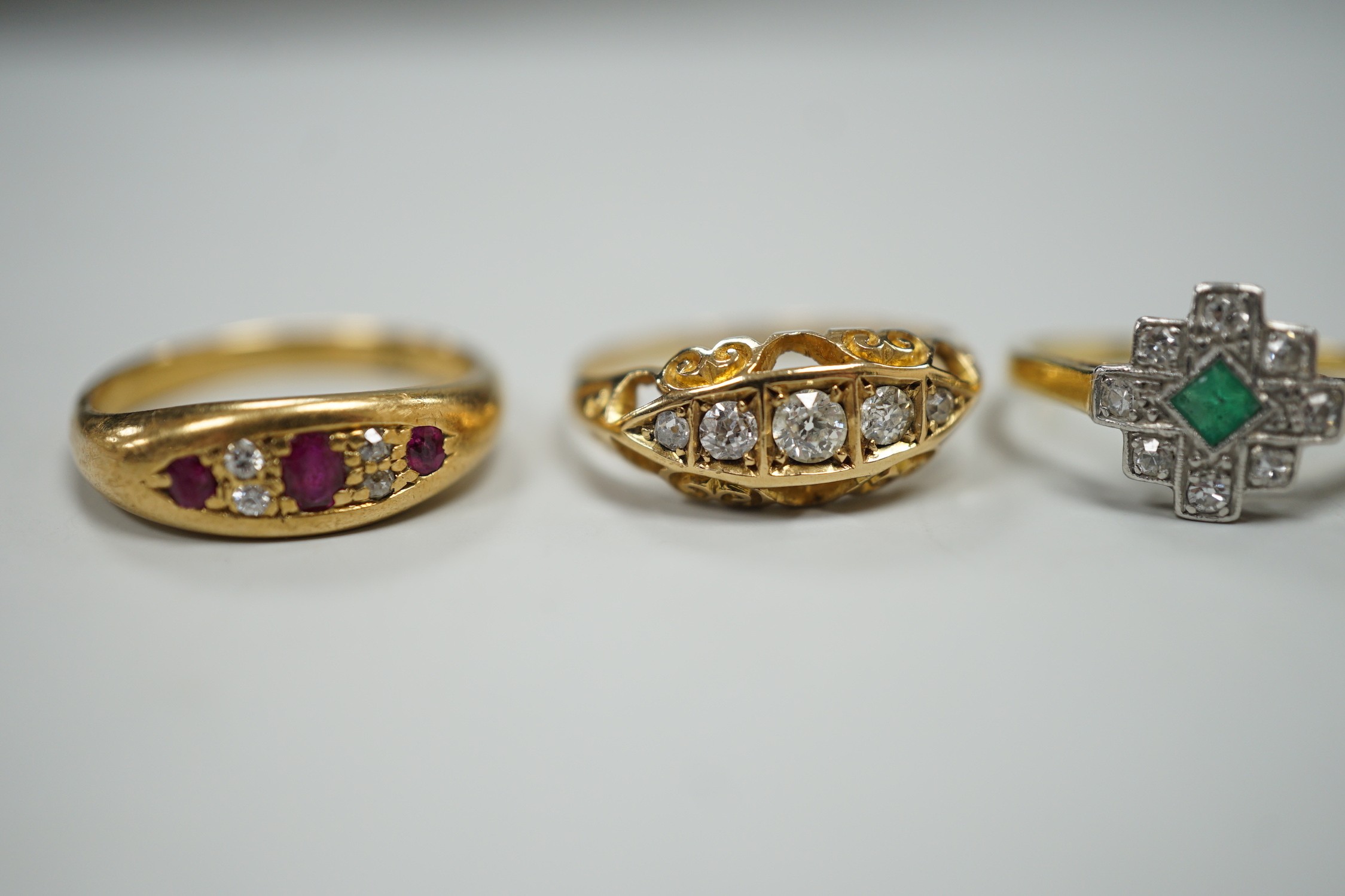 Three early 20th century 18ct and gem set rings, including ruby and diamond chip, size O, graduated five stone diamond, size P and an emerald and diamond cluster, size M, gross weight 10 grams.